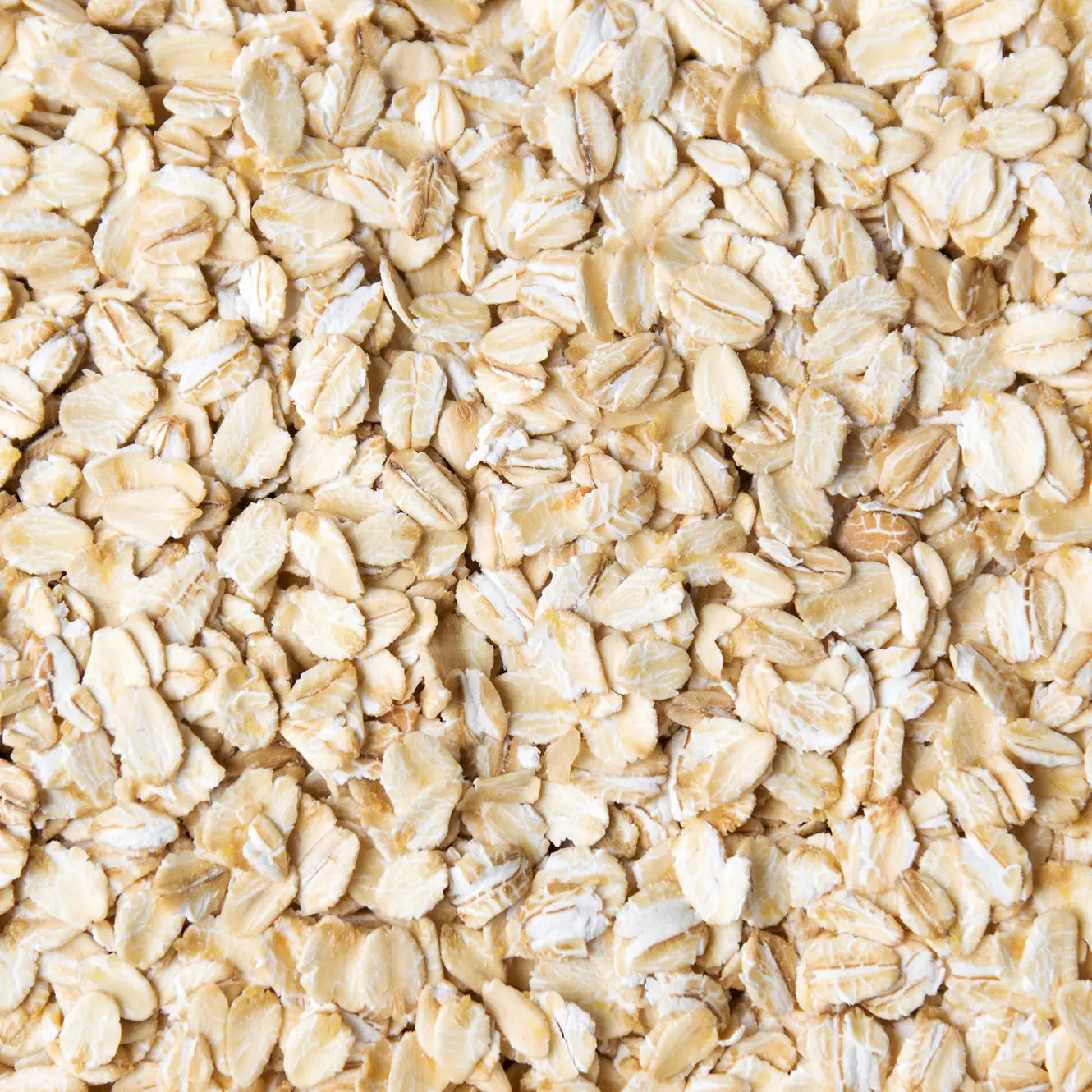 A close-up, top-down view of raw rolled oats filling the entire frame, showing the light beige and cream-colored flat oat leaves.