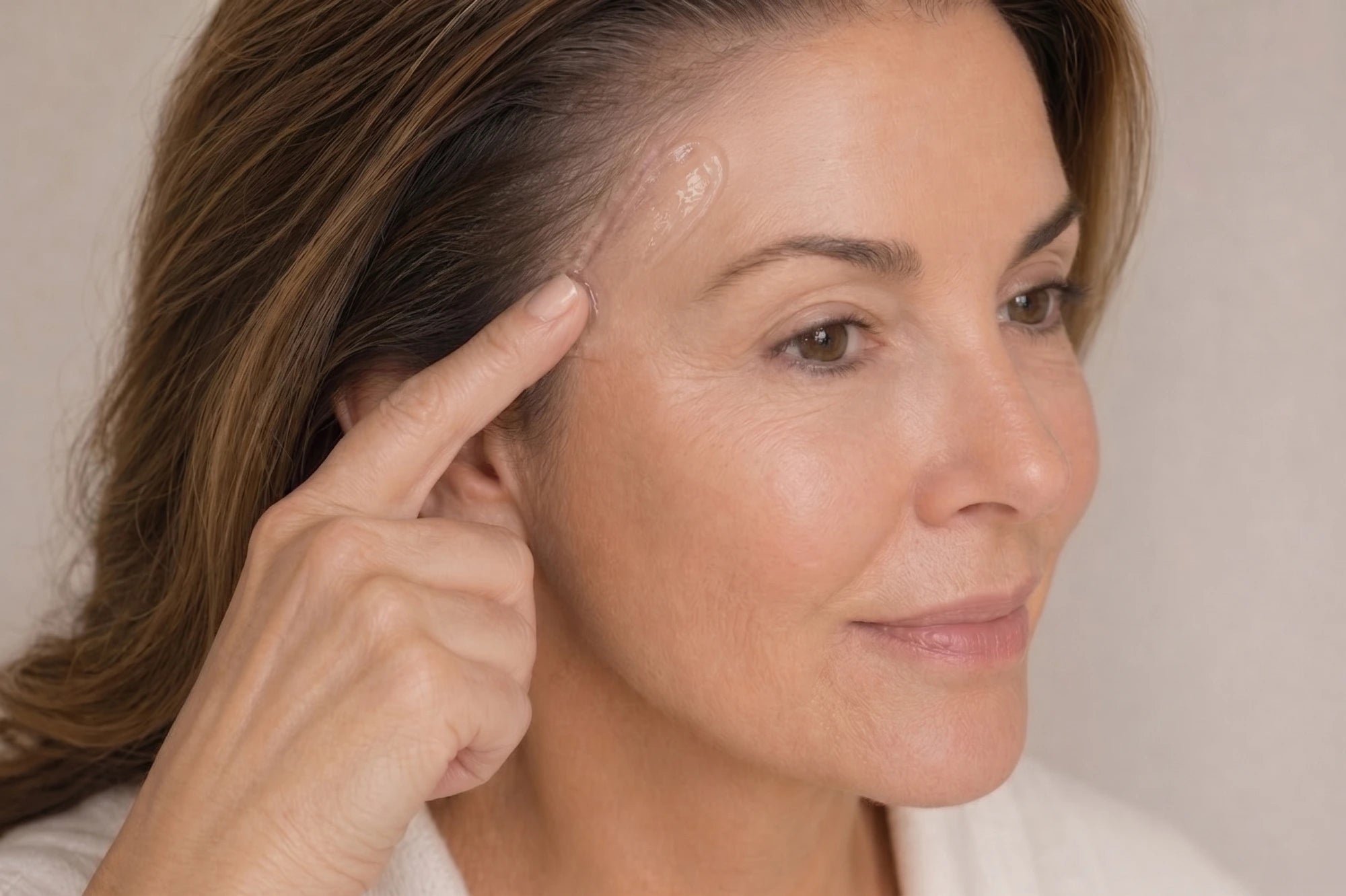 Woman pointing to a blemish on her face against a neutral background
