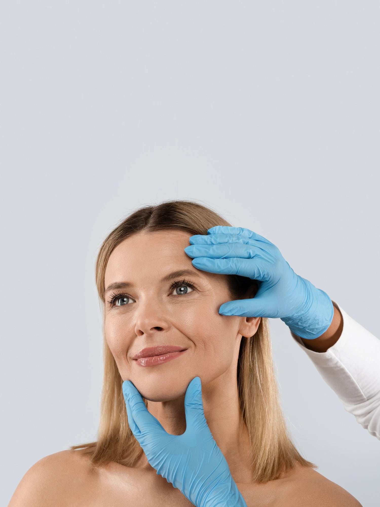 Woman with a skincare professional examining her face against a light gray background