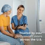 Woman in yellow shirt and headscarf sitting with a healthcare professional in blue scrubs, discussing something on a tablet.