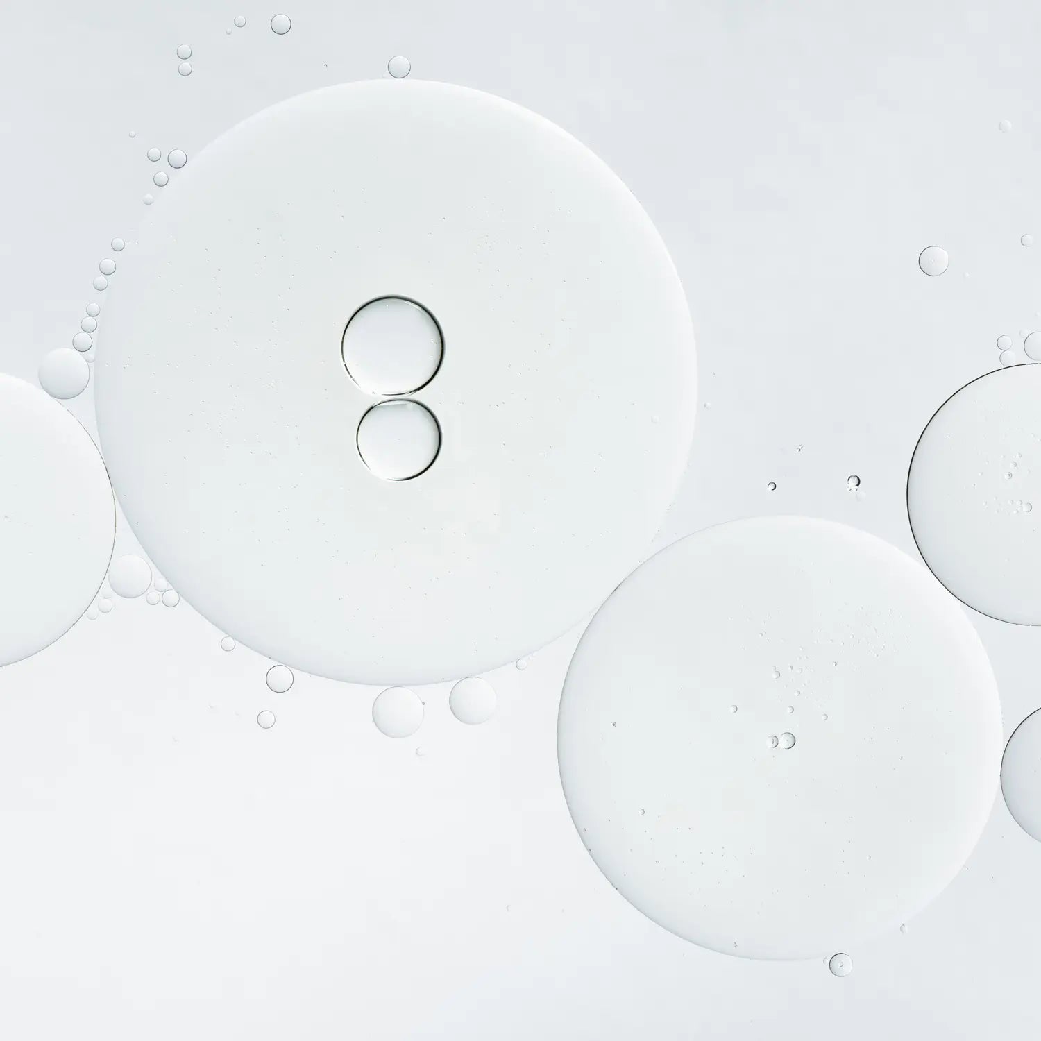 A close-up abstract view of translucent circular droplets and bubbles on a very light gray to white background.