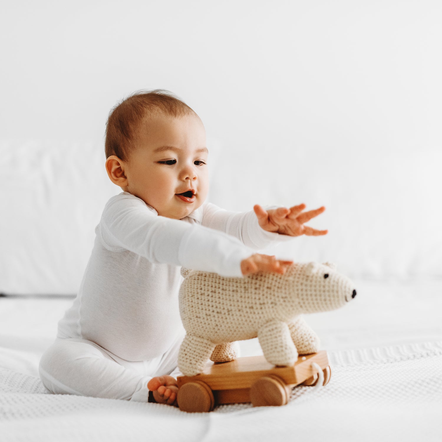 close up of a baby boy smiling and playing with a stuffed animal on the bed wearing Rejuvaskin's eczema clothing line, seamless moisture wicking baby sleepsuit