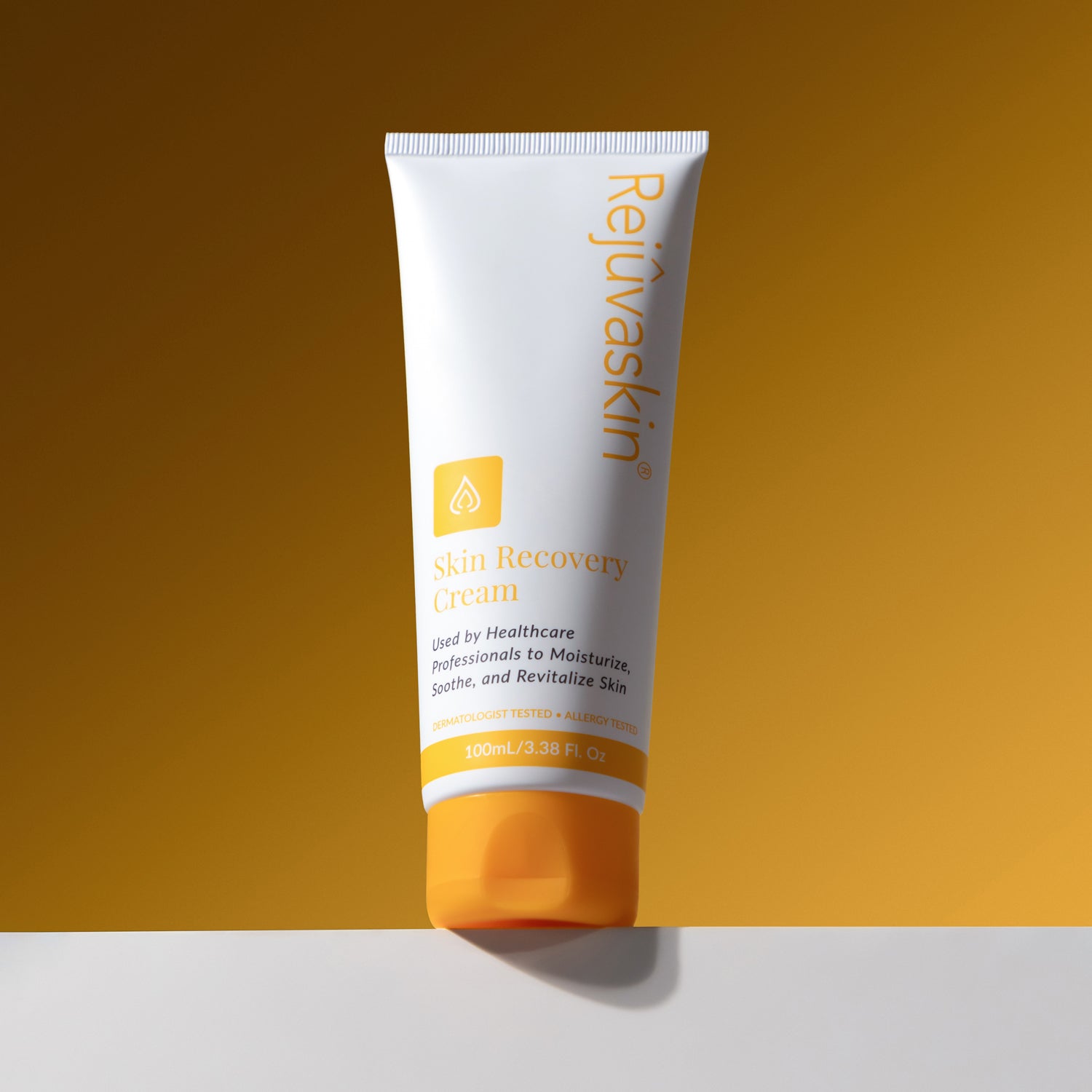 A 120 mL white squeeze tube of Rejuvaskin Skin Recovery Cream with an orange cap, standing on a white surface against a warm golden-brown gradient background.
